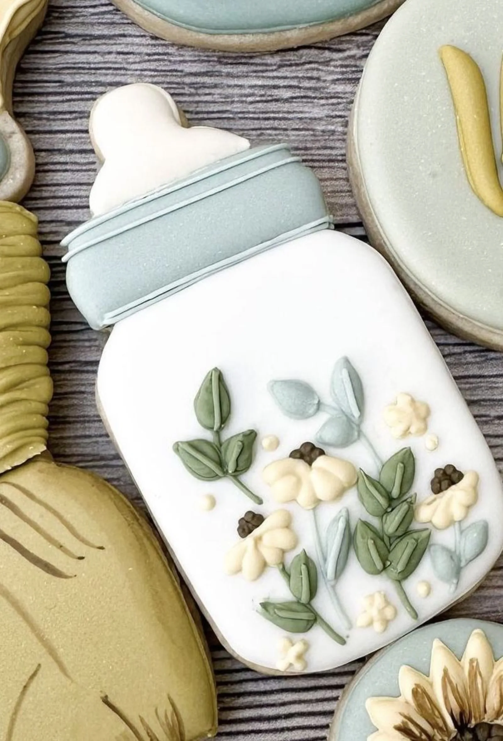 Baby shower cookies shaped like a bottle and a mason jar with piped greenery and white flowers.