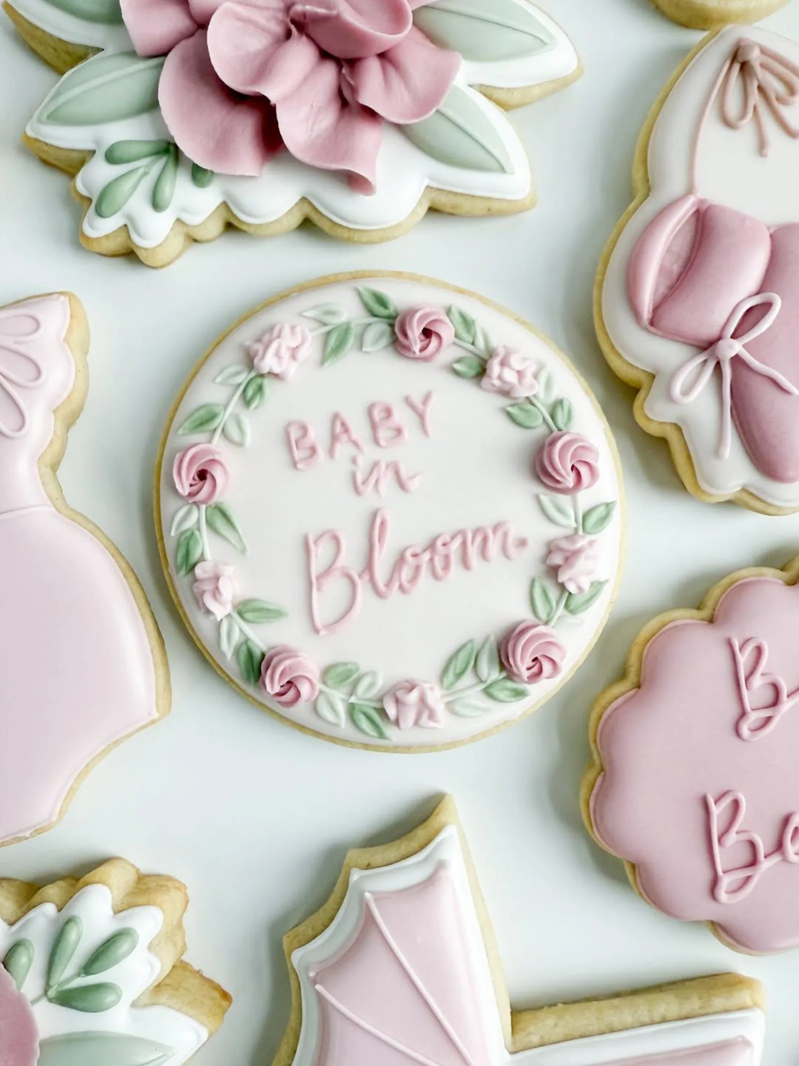 Baby in Bloom wreath cookie in pink and green with a bow and dress shaped cookies.