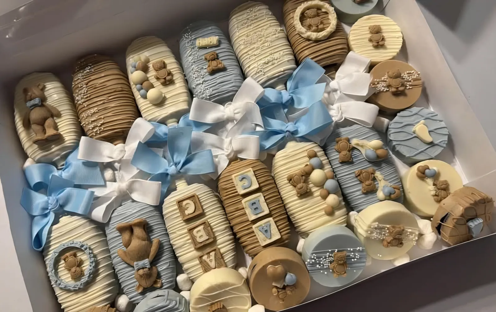 Assorted chocolate-dipped treats decorated with blue and white ribbons, teddy bears and alphabet blocks.