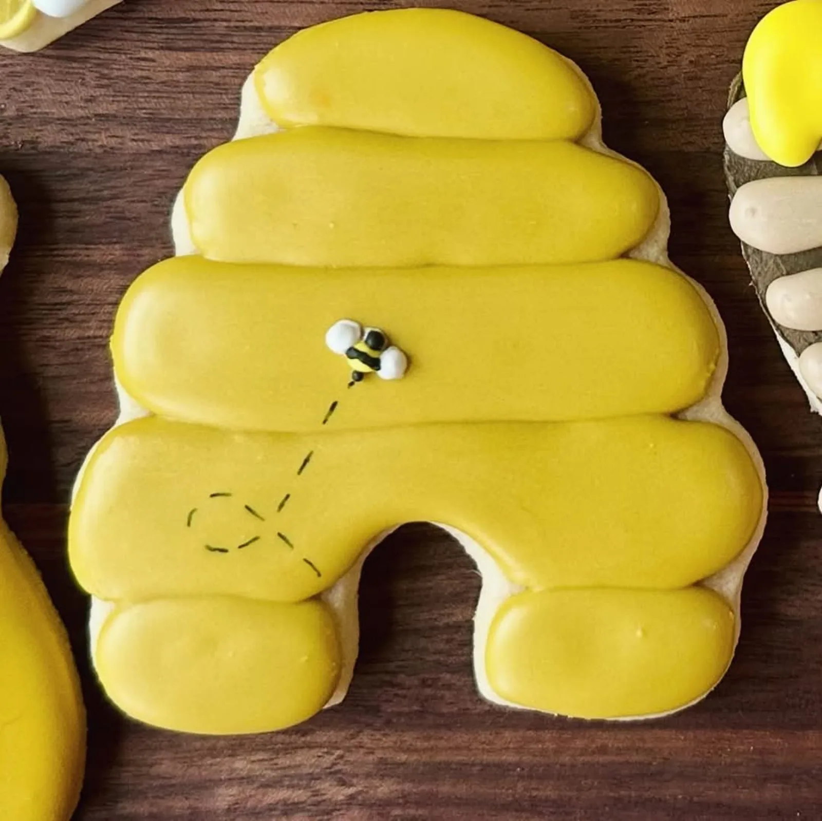 Close up of a yellow beehive cookie with a piped bee and a dashed flight path.
