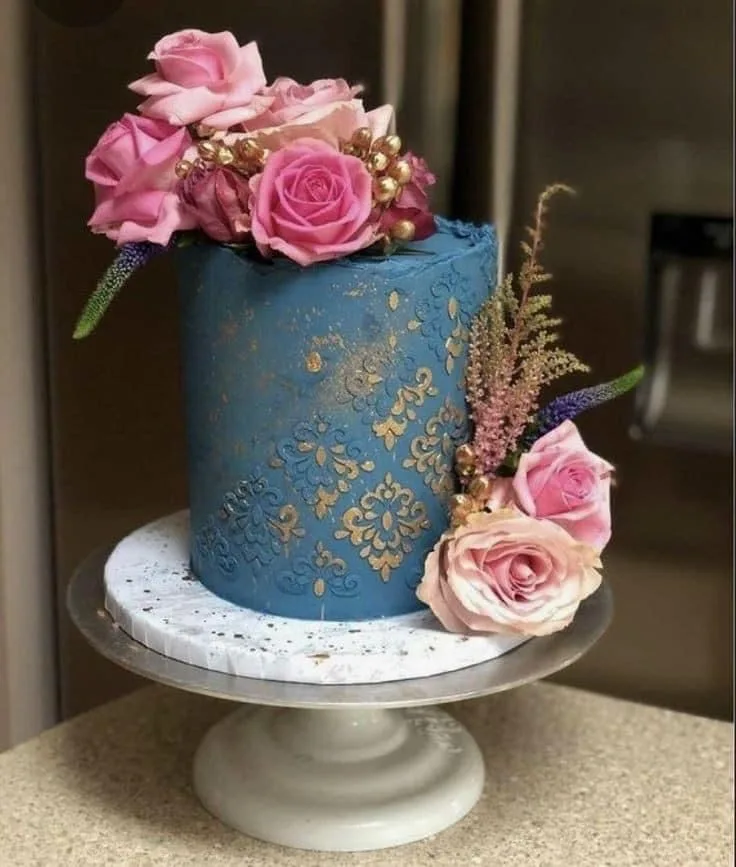 Tall single tier blue cake with gold damask pattern, topped with pink roses and gold berries, accented with pink heather and lavender.