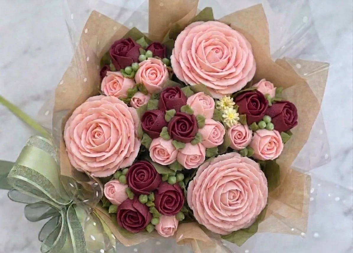 Cupcake bouquet wrapped in brown paper and cellophane, featuring large pink and small burgundy rose-shaped frosting piped on cupcakes.