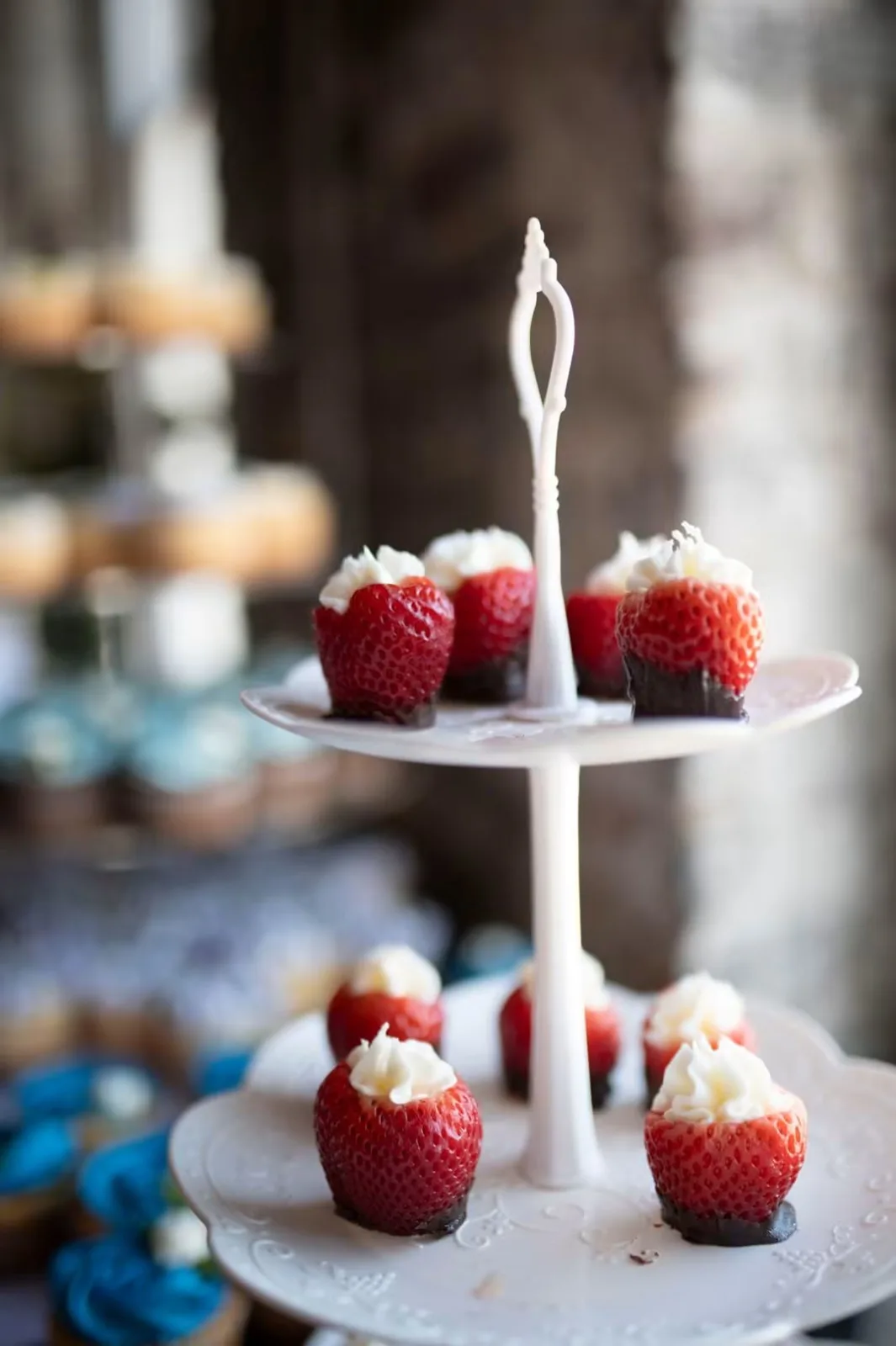 Strawberries dipped in dark chocolate and filled with piped cheesecake cream on a two-tier white stand.