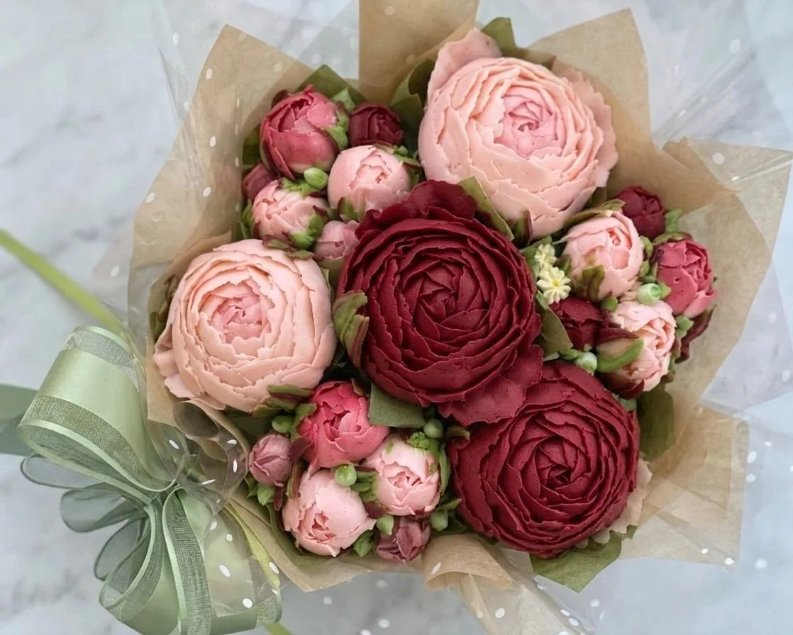 Edible frosting bouquet piped into pink and burgundy rose blooms, wrapped in brown paper and cellophane with a green ribbon bow.