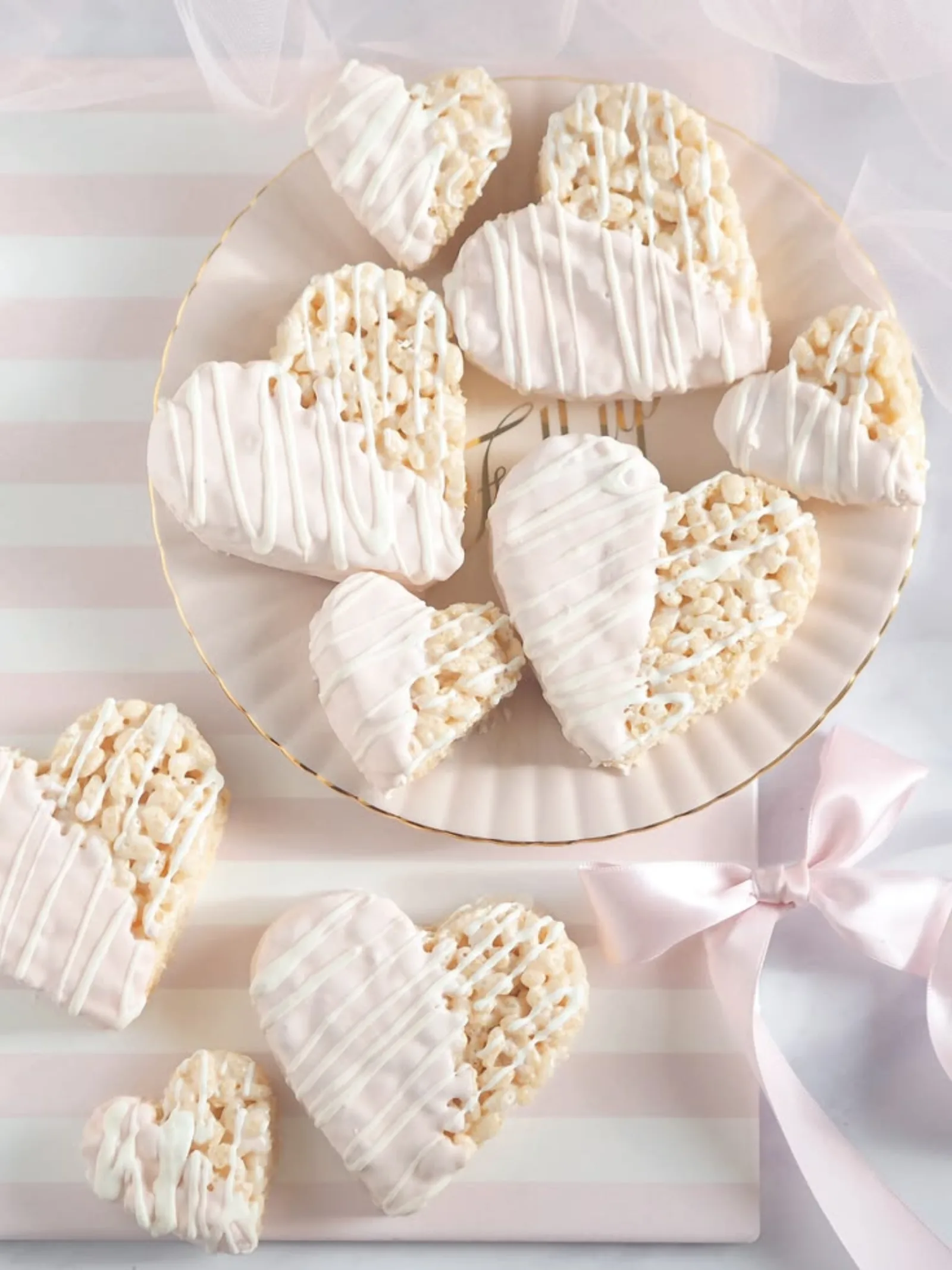Heart-shaped rice krispie treats dipped in white chocolate with drizzle detail, arranged on a pink cake stand.