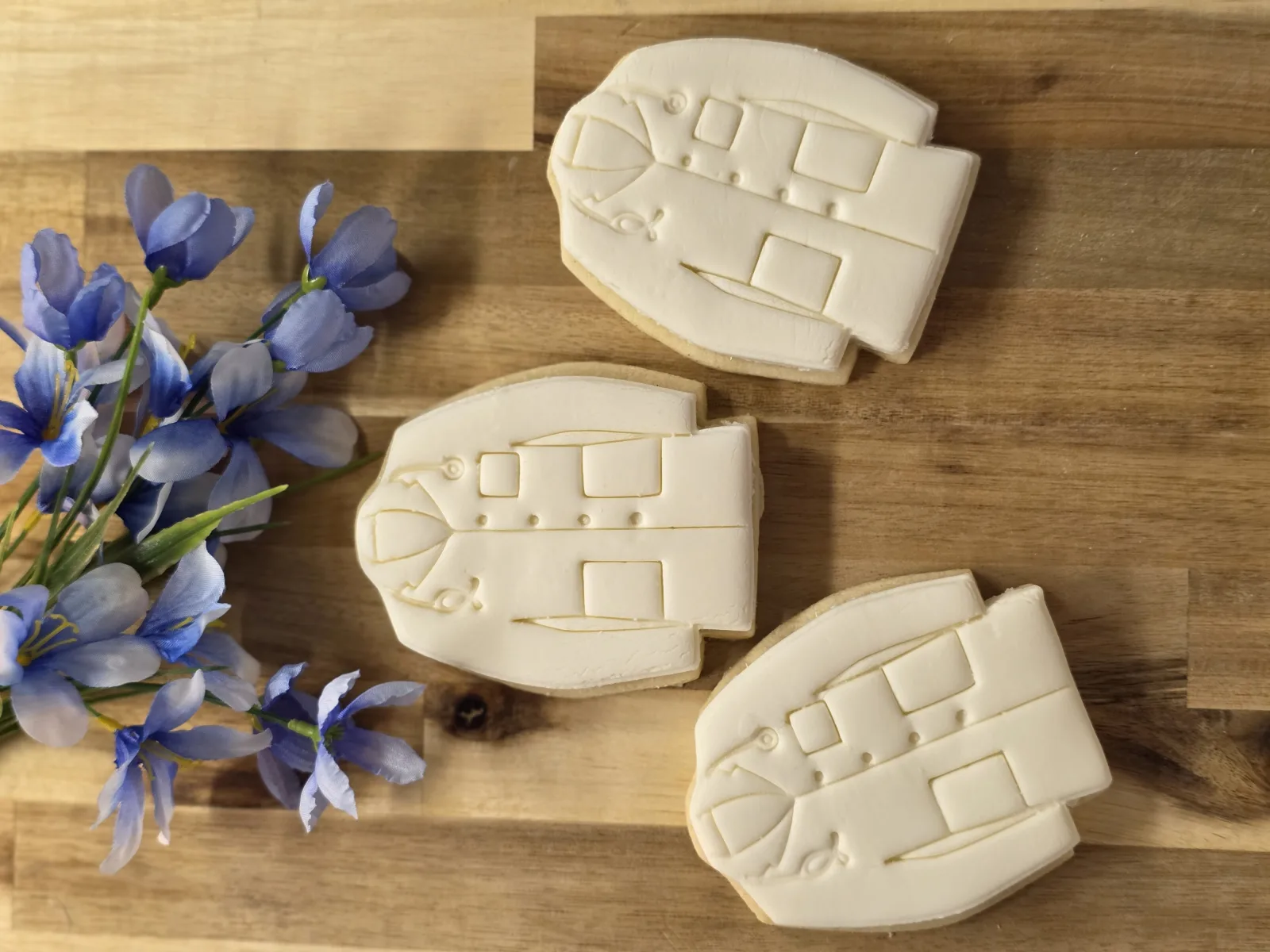 Three cream colored sugar cookies with embossed panel detailing on a wood board beside blue iris blooms.