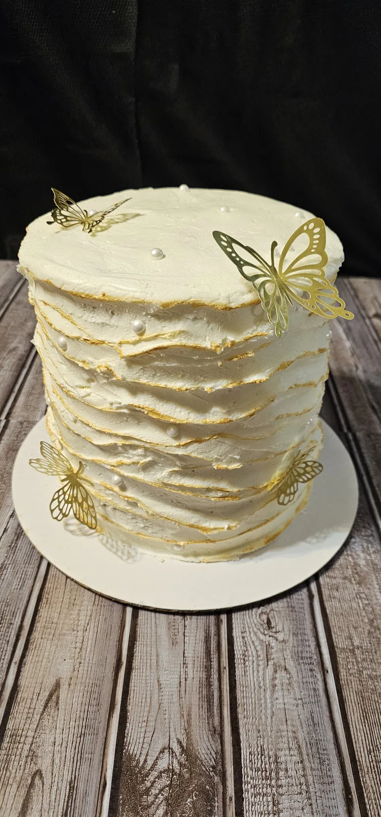 Tall white buttercream cake with rustic textured ridges edged in gold, adorned with gold butterfly toppers and small white pearl accents.