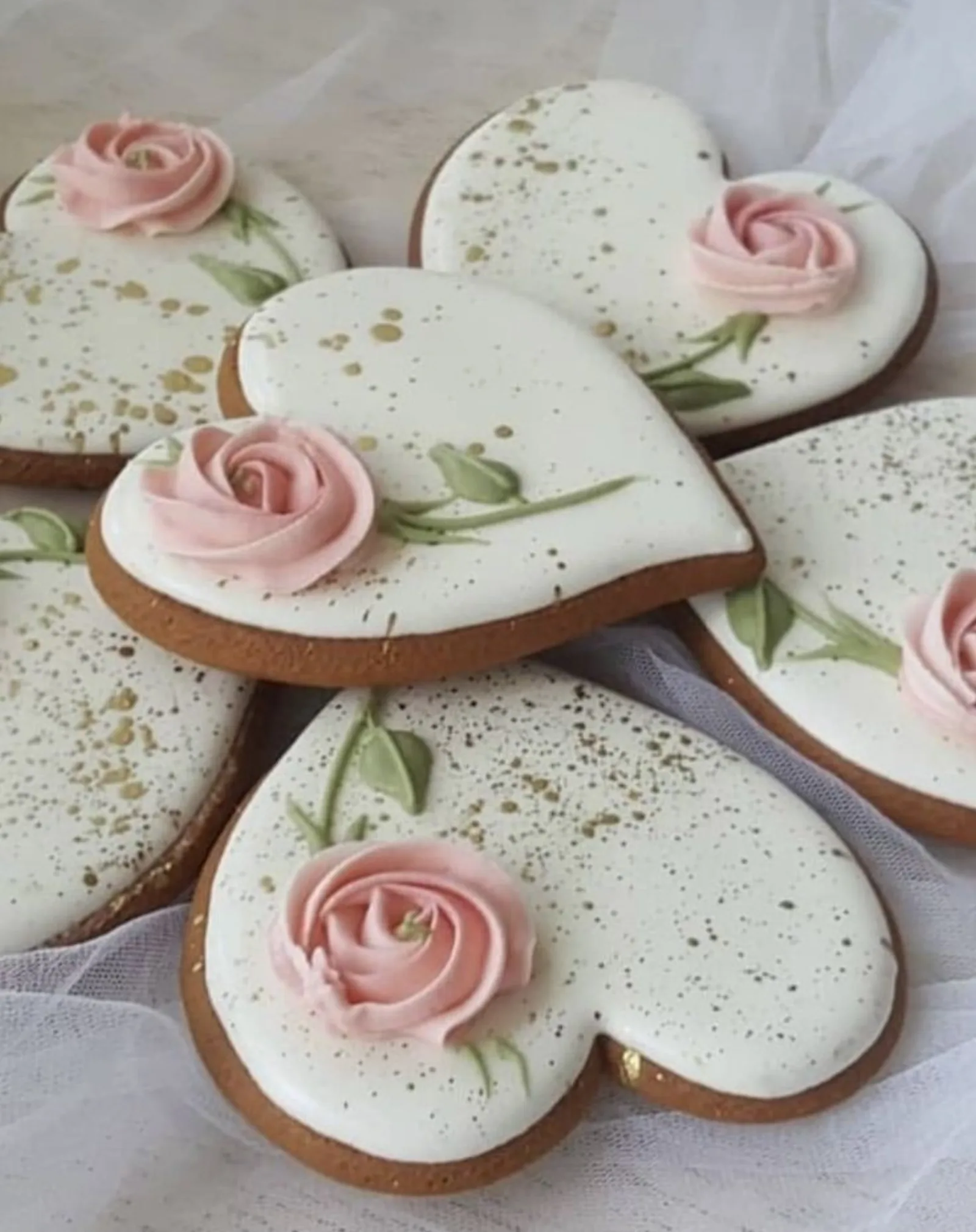 White heart cookies with gold speckles and piped pink roses on sheer fabric.