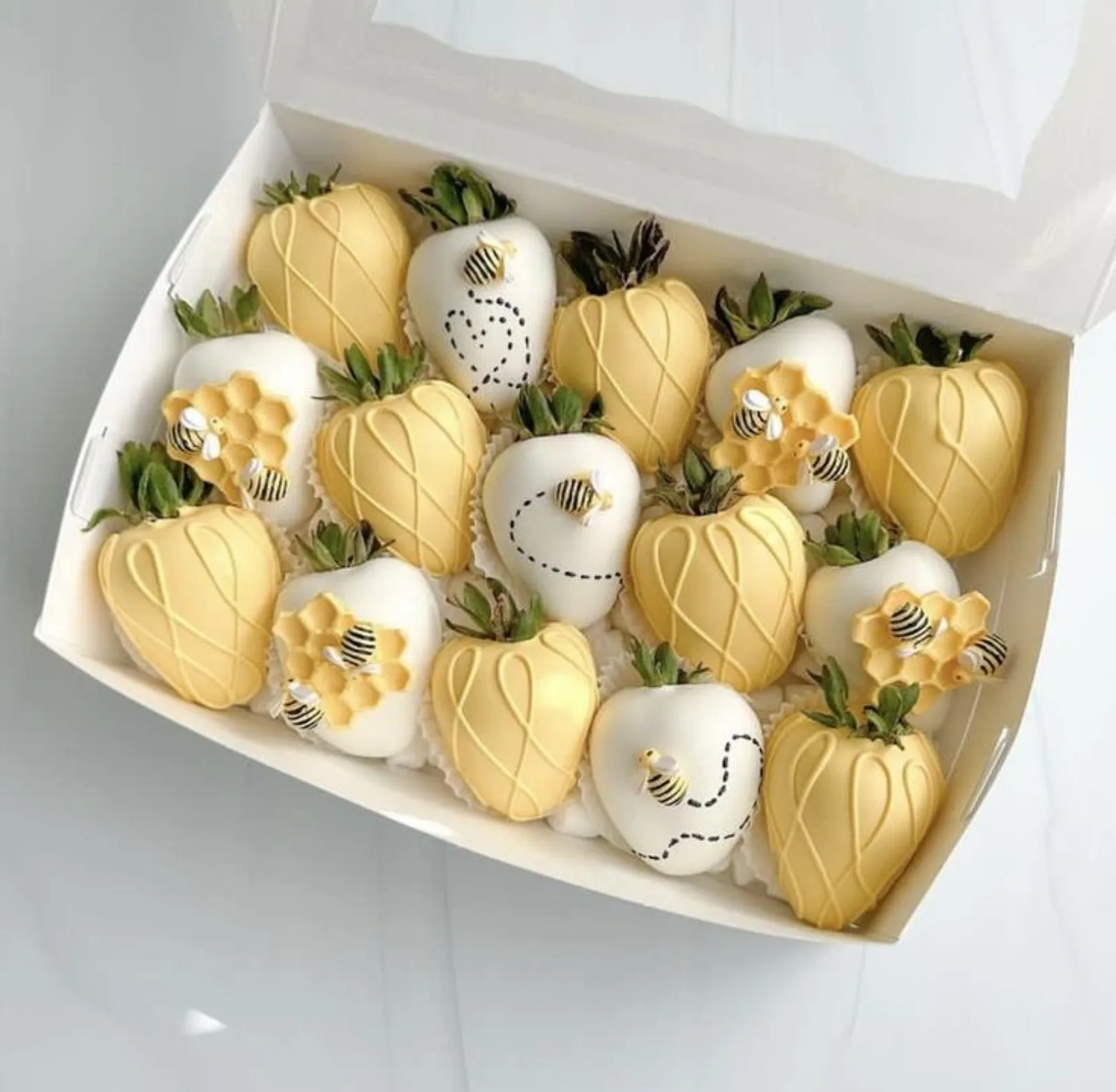 Chocolate-covered strawberries with white and yellow chocolate stripes, fondant bees and honeycomb pieces, viewed from above.
