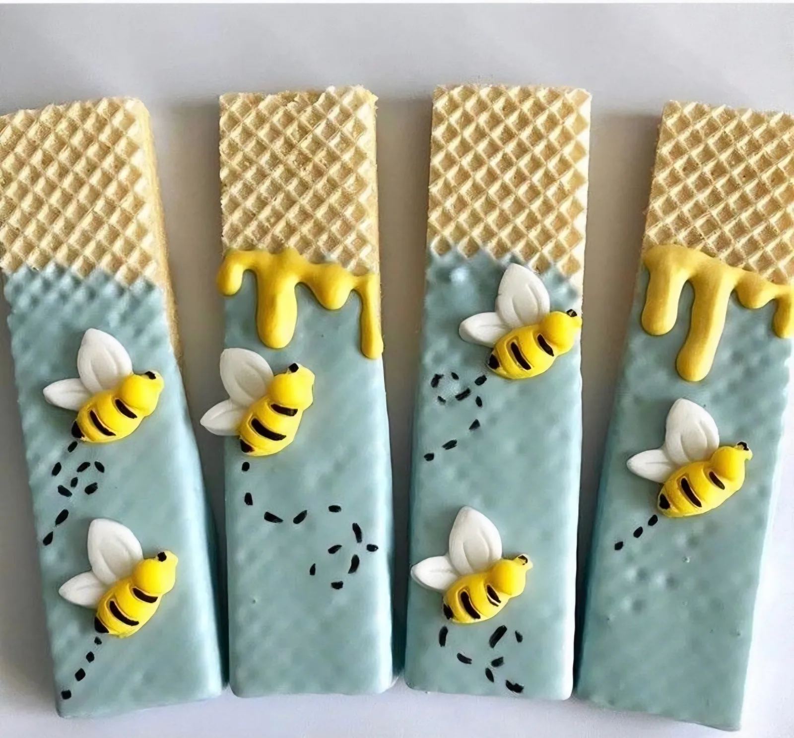 Wafer cookie sticks dipped in pale blue chocolate with a honey drizzle top and fondant bees flying up the stick.