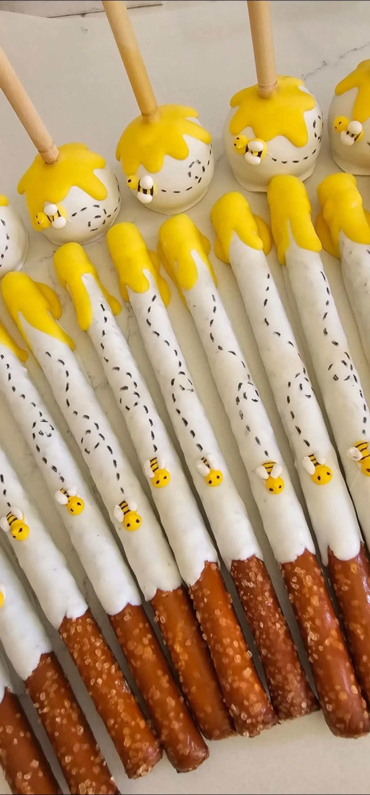 Honey and bee themed marshmallow pops on wooden honey-dipper sticks, decorated with fondant bees and honeycomb.