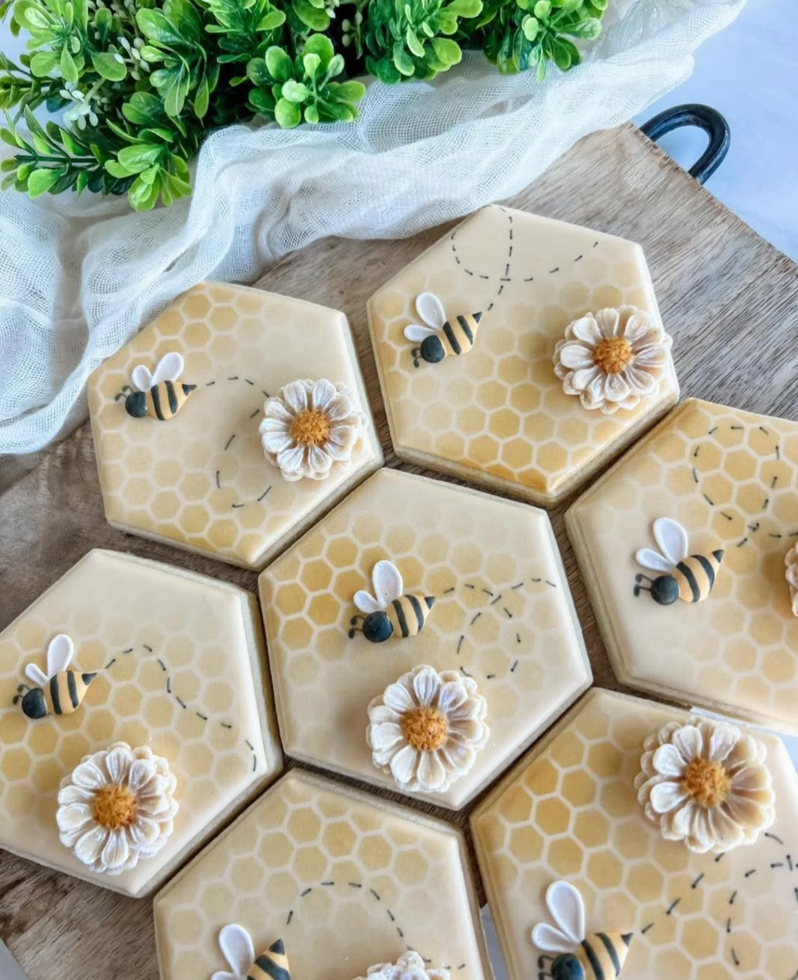 Honeycomb hexagon cookies iced in gold and cream with bees and white daisies, styled with greenery.