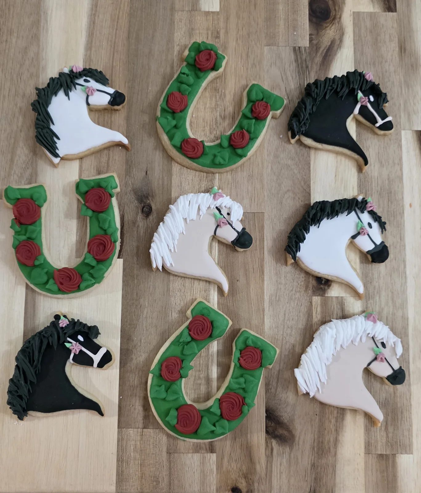 Decorated sugar cookies featuring horse heads with detailed manes, bridles, and pink roses alongside green horseshoe cookies adorned with red roses and green leaves.