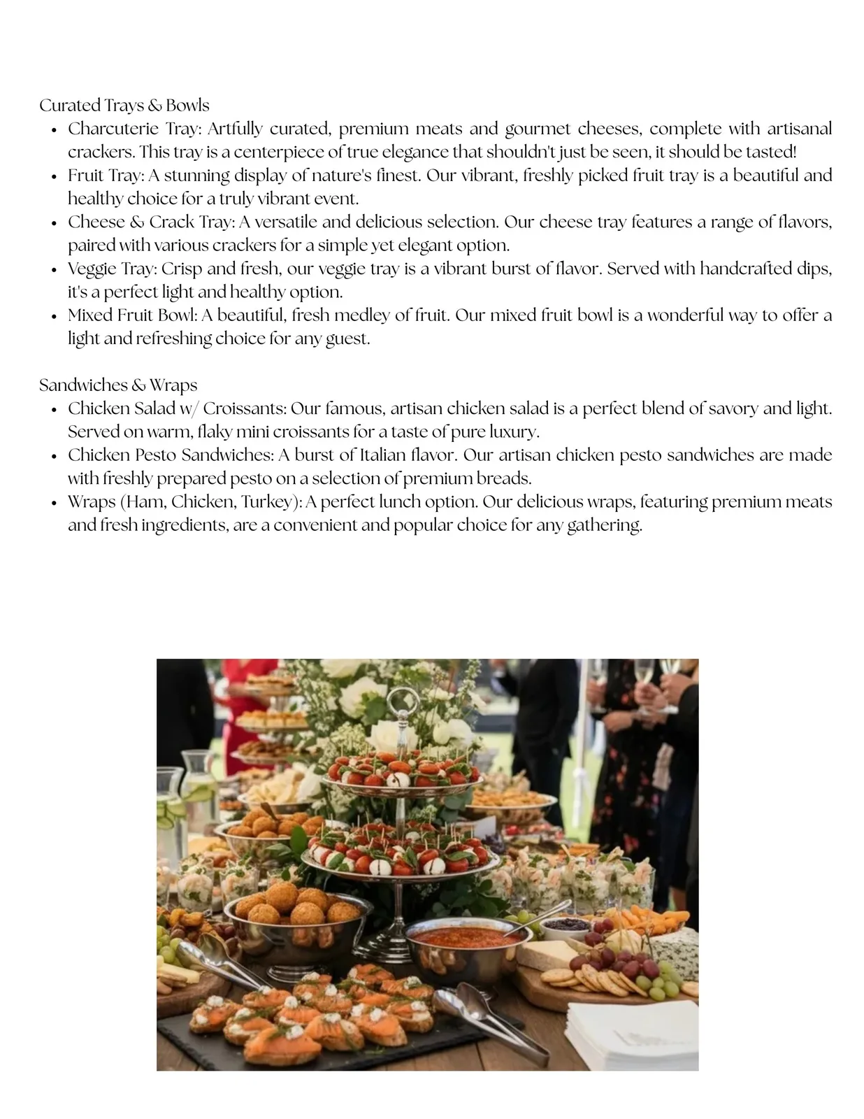 Catered grazing table with tiered caprese skewers, crostini, fried bites, cheese, crackers, grapes, and guests holding glasses.