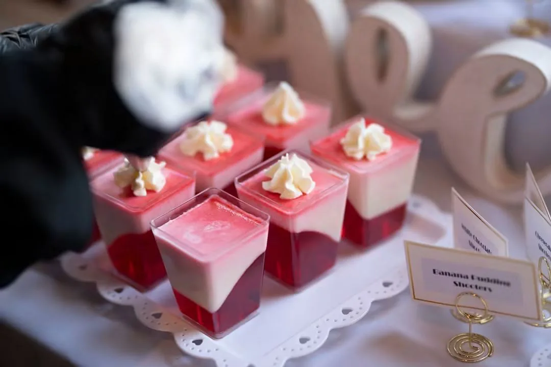 Layered dessert shooters of red gelatin and cream topped with whipped cream, beside labeled dessert cards.