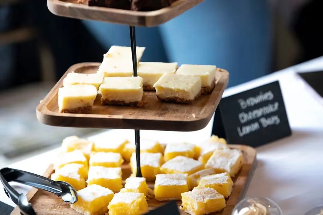 Lemon bars, cheesecake bars and brownies on a three-tier wooden stand with a chalkboard label.