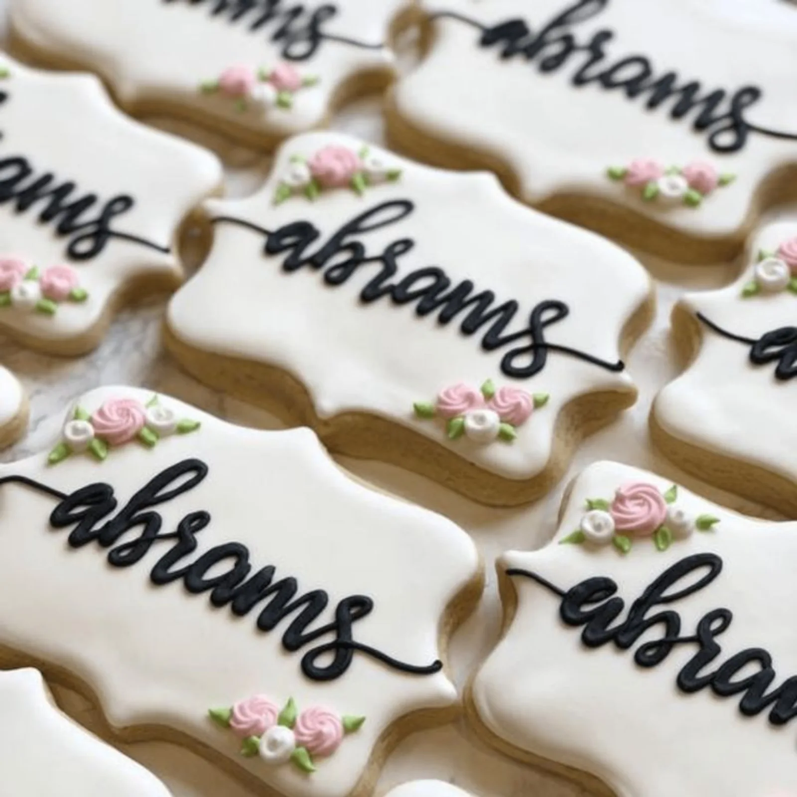 White plaque cookies piped with a family name in black script and small pink roses.