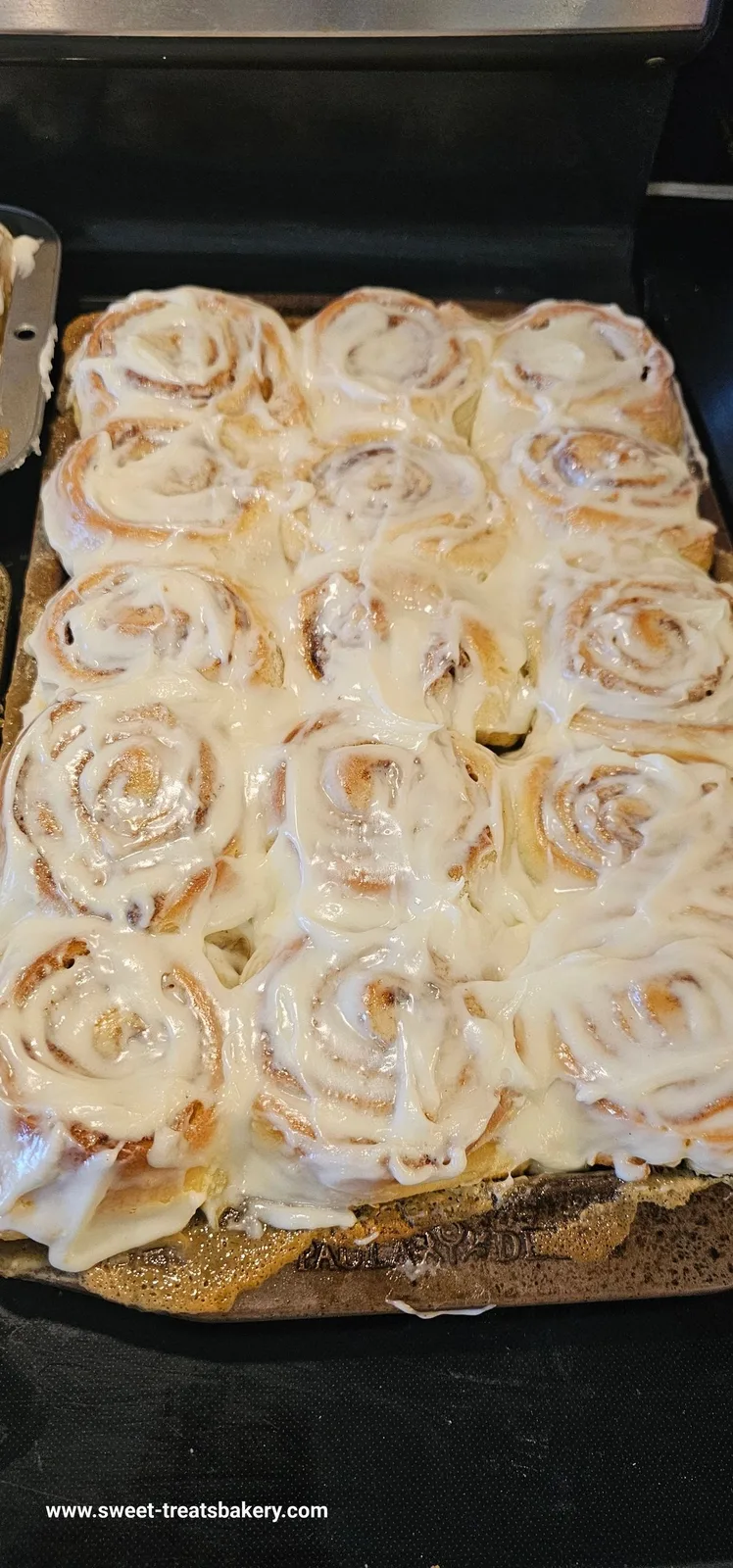 A pan of freshly baked cinnamon rolls topped with thick white icing, with a knife resting on the left edge.
