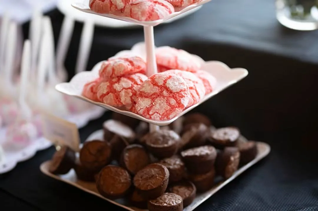 Pink crinkle cookies on a tiered stand above a tray of chocolate brownie bites.