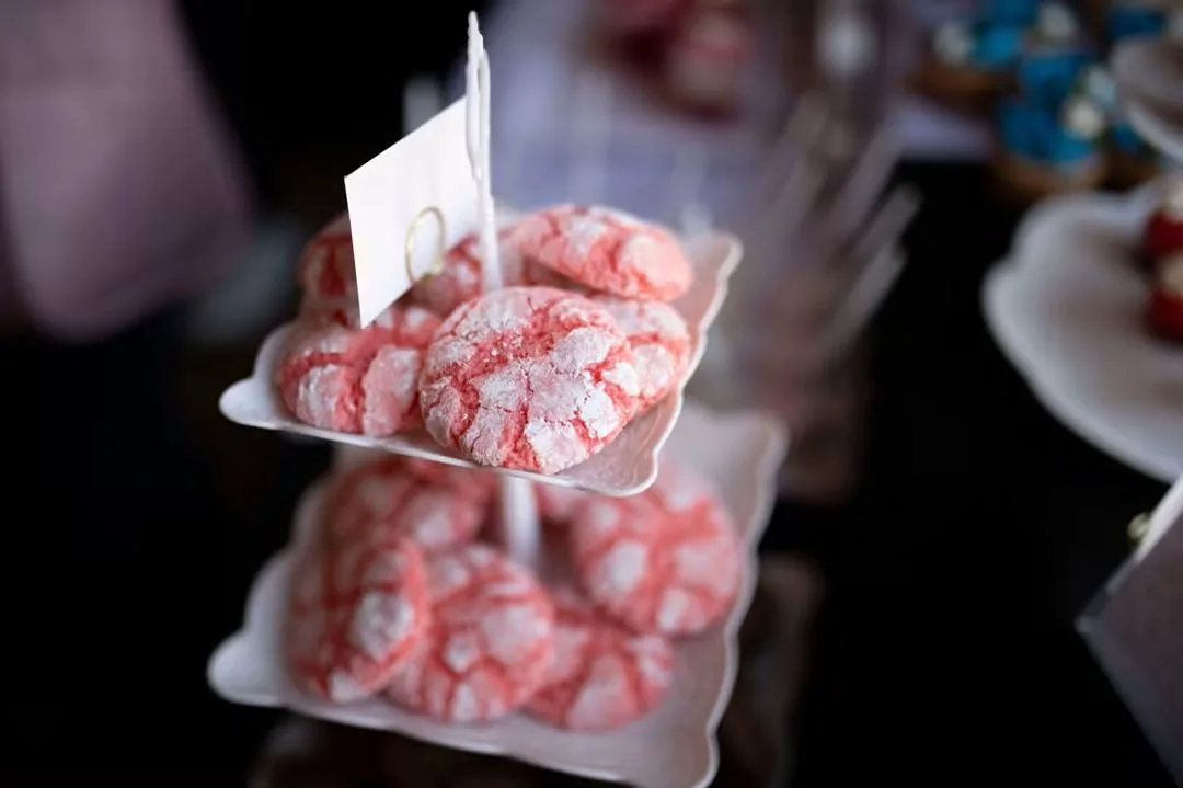 Pink crinkle cookies dusted with powdered sugar on a two-tier white stand.