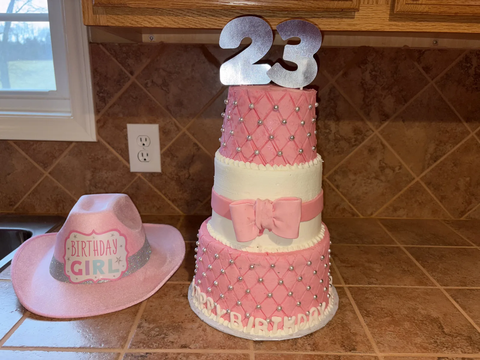 Three tiered pink and white cake featuring quilted pattern with silver bead accents, a pink fondant bow, and a silver number 23 topper.