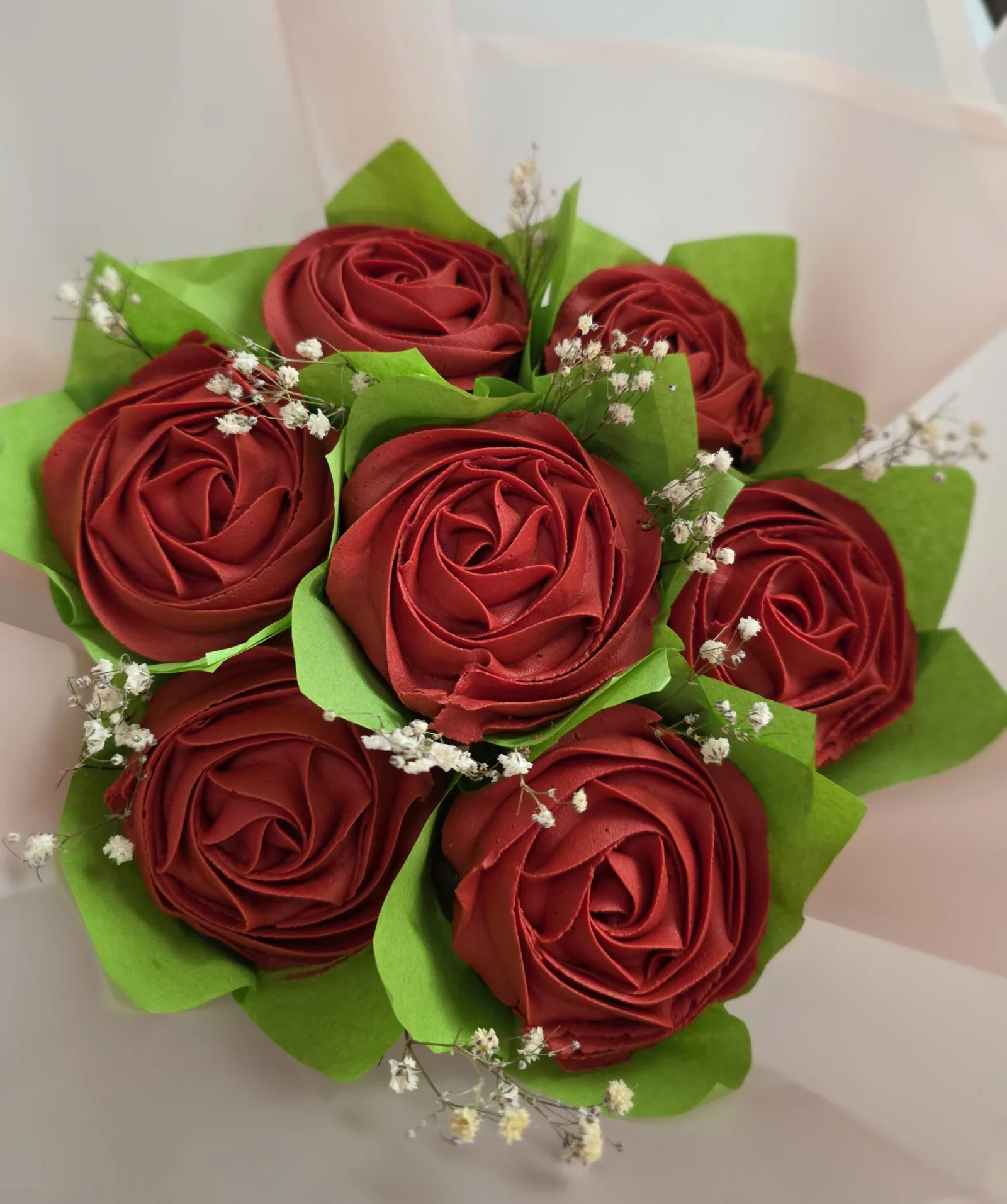 Cupcake bouquet of deep red buttercream roses with green tissue leaves and dried baby's breath, wrapped as a gift.