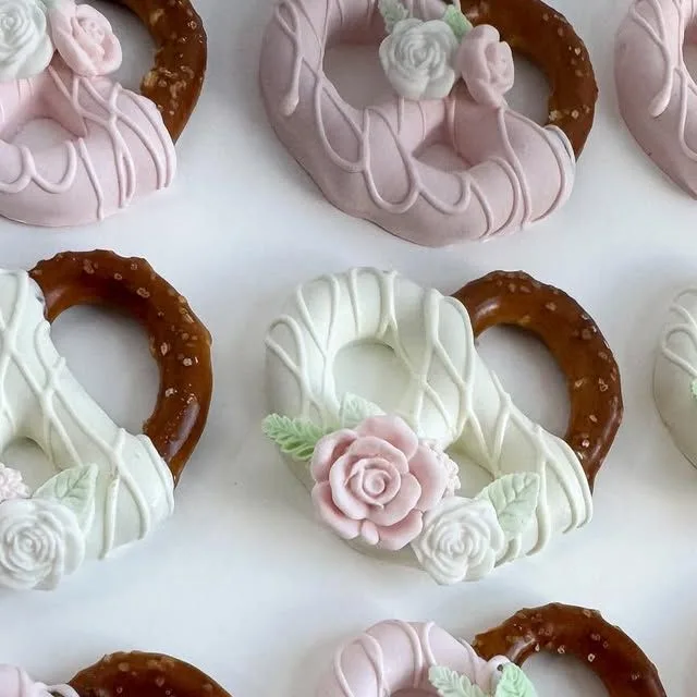 Pretzels dipped in pink and white chocolate with drizzle, decorated with small pink and white candy roses.