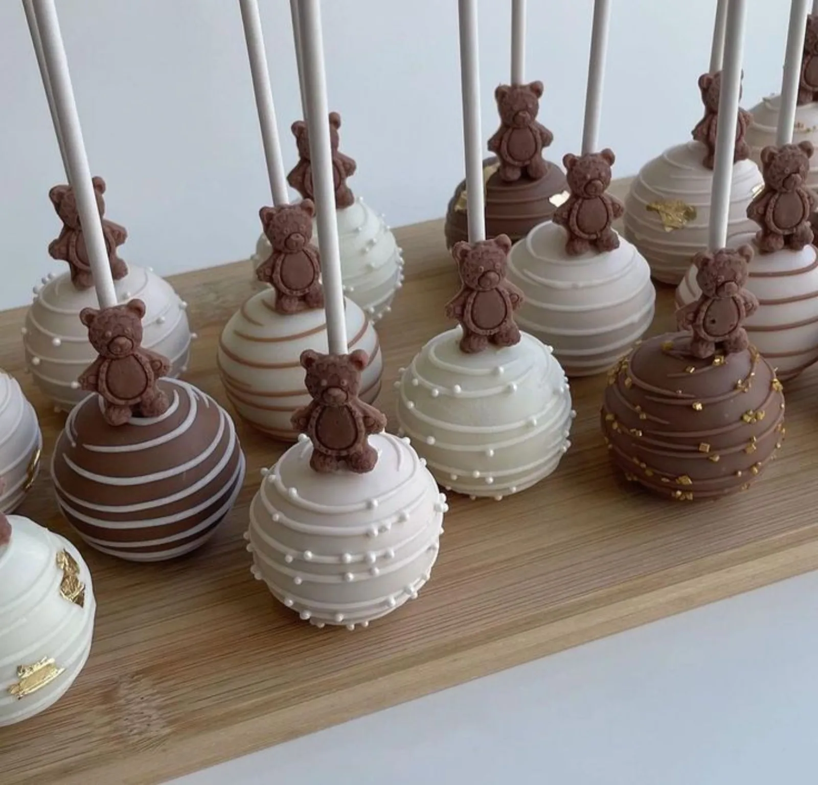 Round chocolate-dipped cake pops in neutral cream and brown tones topped with chocolate teddy bear figures.