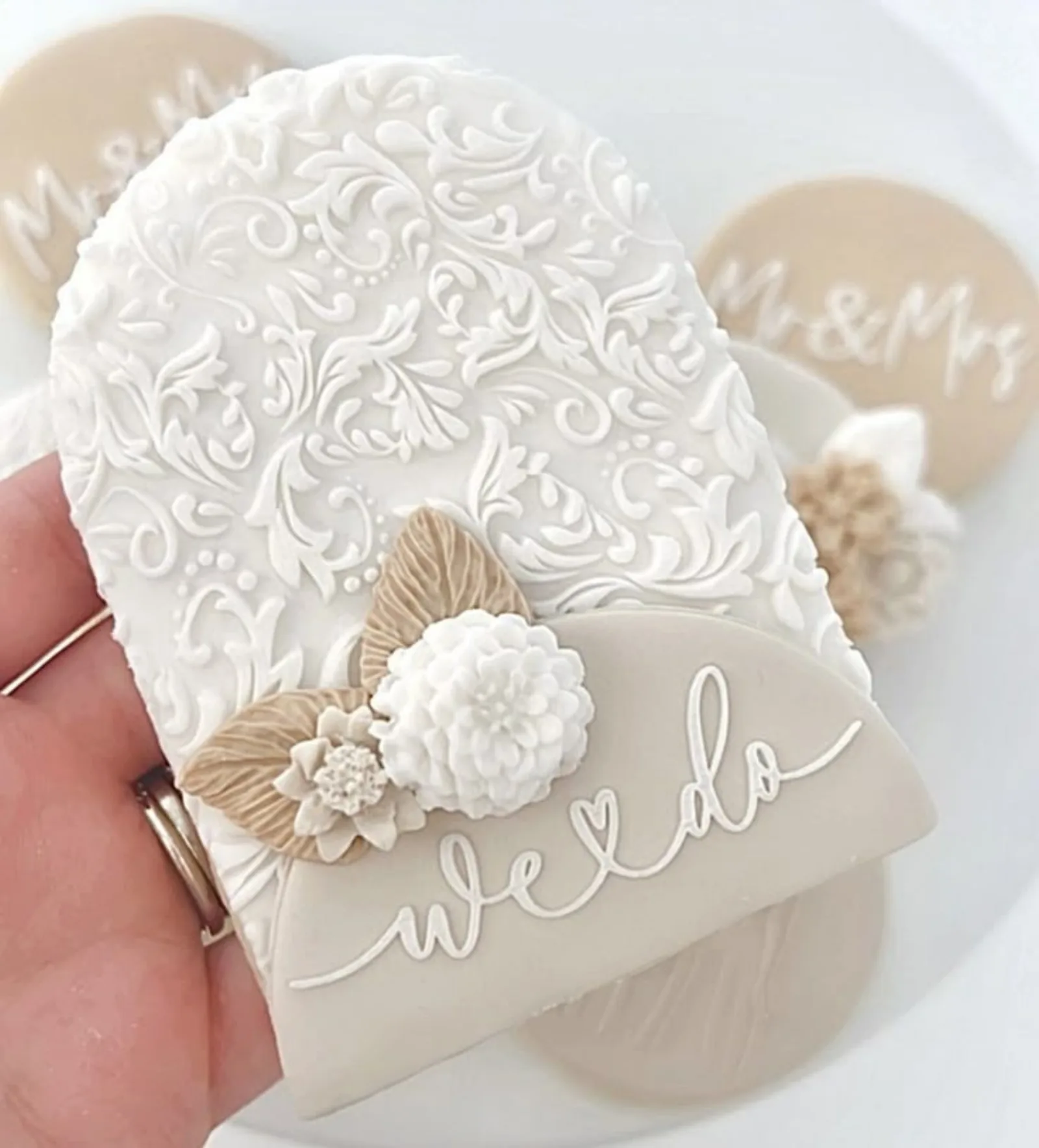Hand holding a textured white arch cookie reading we do, finished with piped flowers.