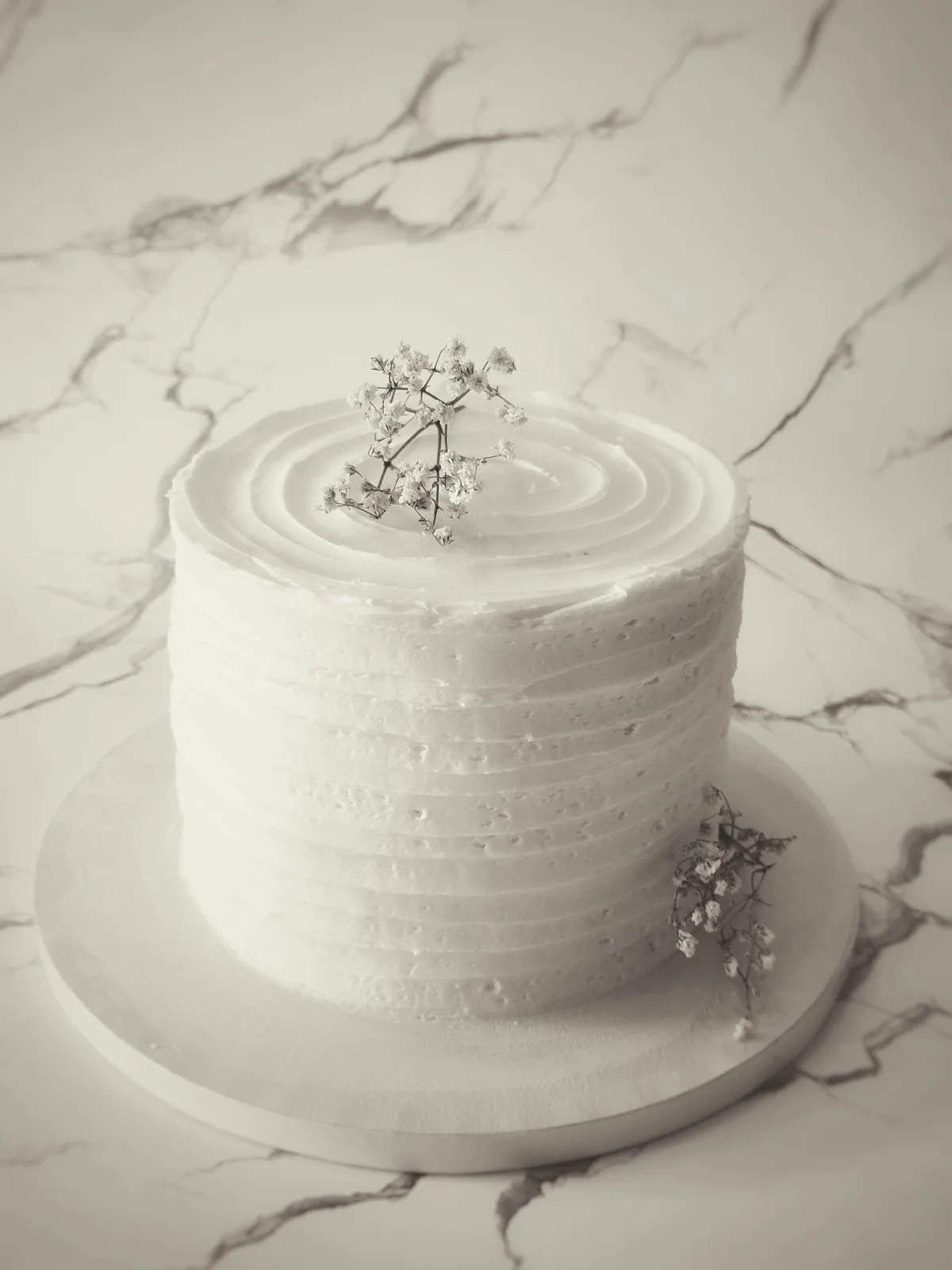 A single tier white frosted wedding cake with textured ridges on the sides and a smooth swirled top, decorated with delicate baby's breath flowers.