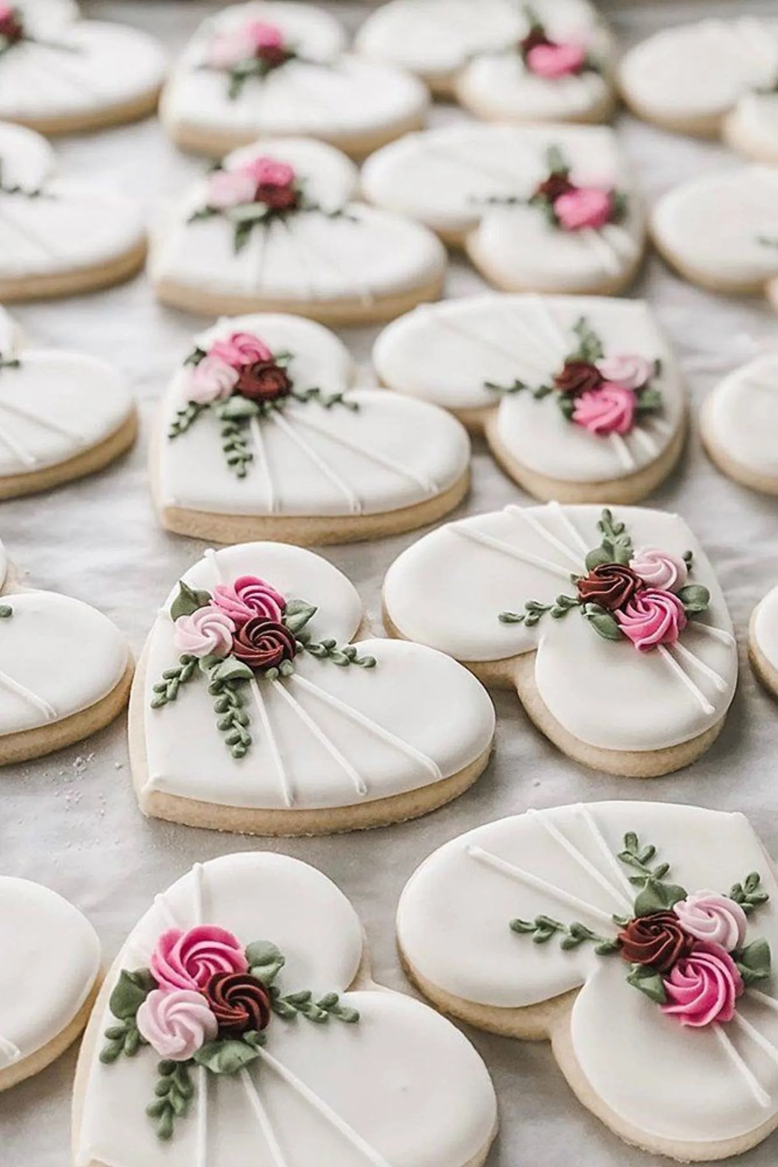 White oval and heart cookies piped with pink and burgundy roses and green leaves.