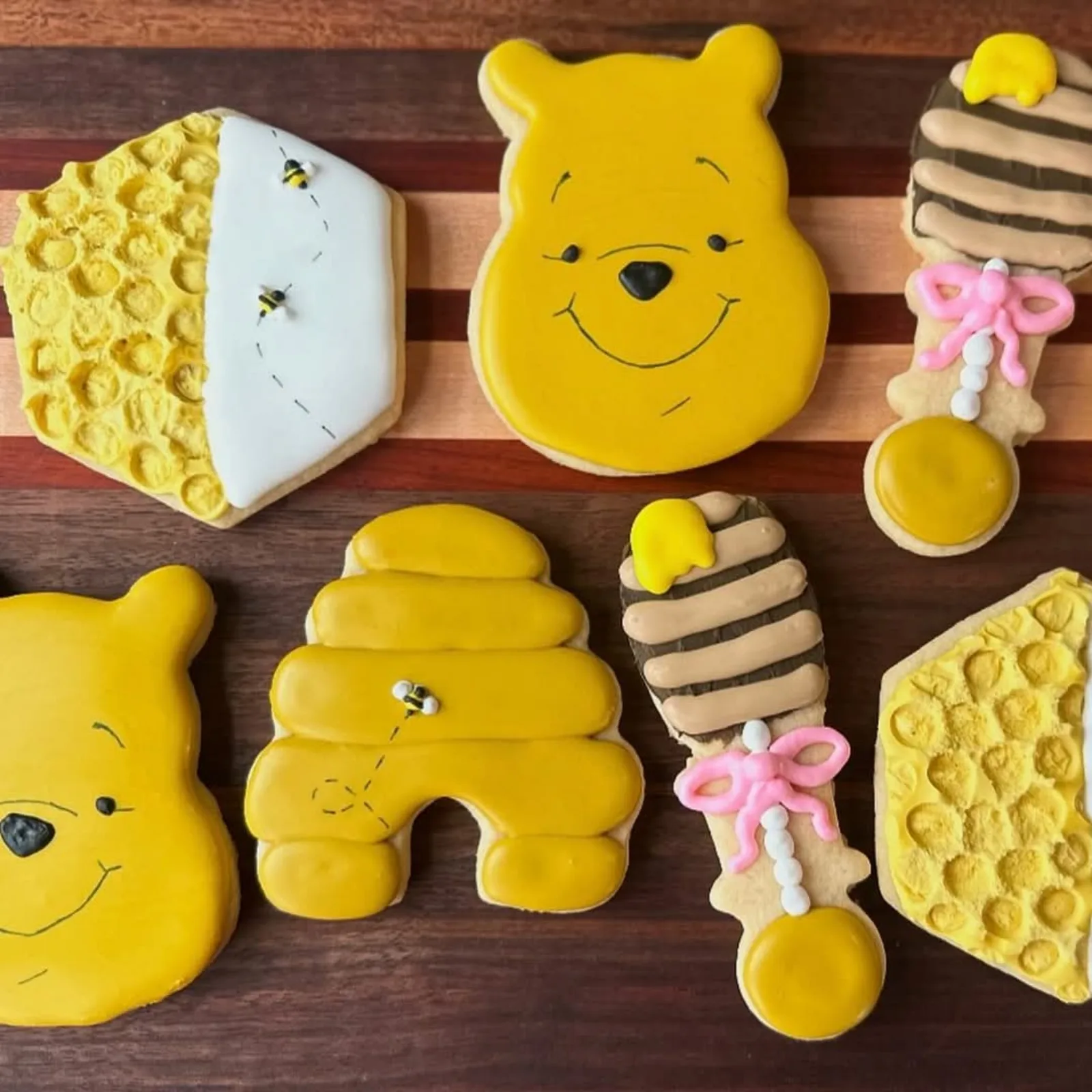 Winnie the Pooh cookie set with a bear face, beehives, honey dippers and honeycomb hexagons on a wood board.
