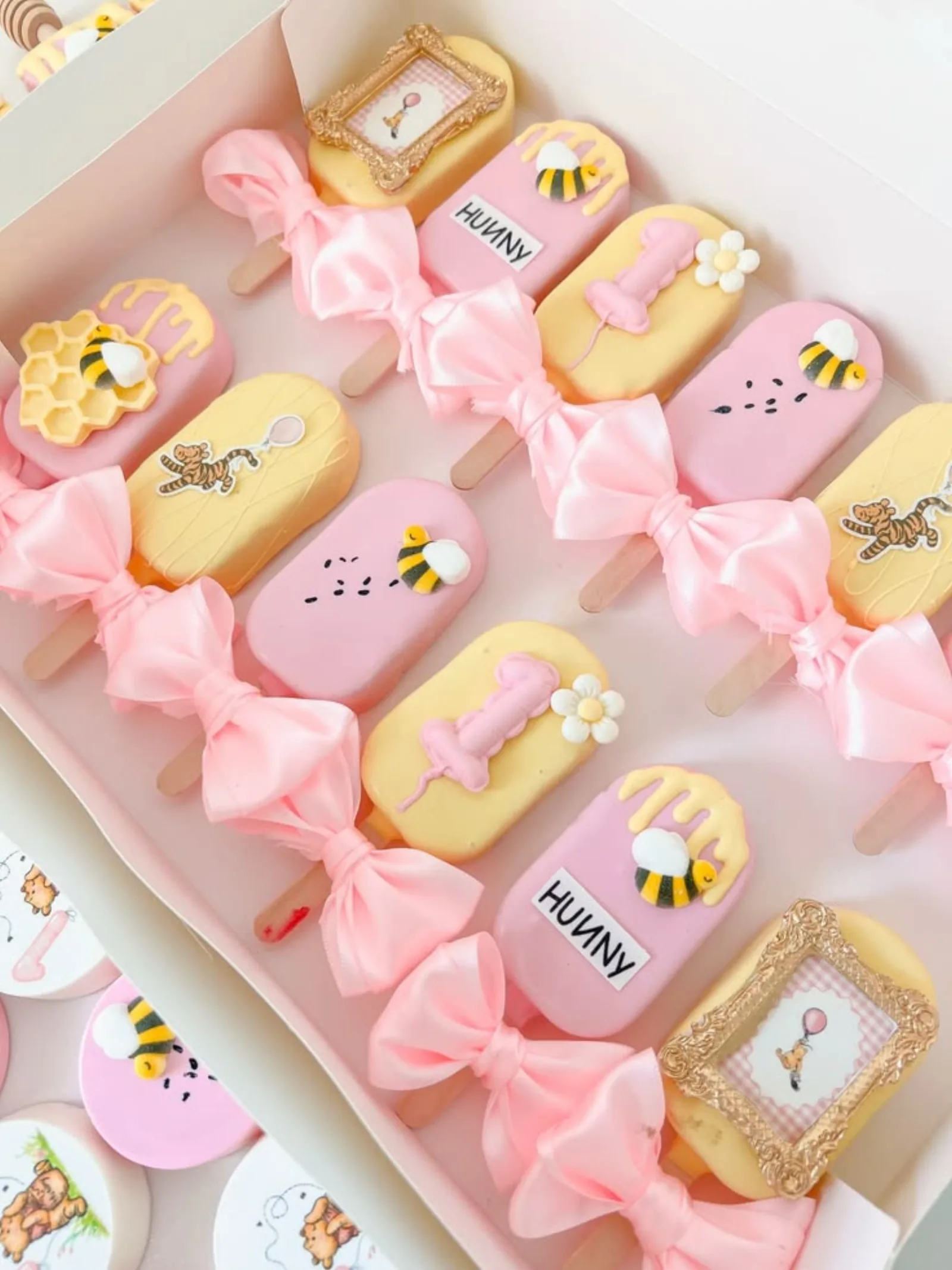 Pink and yellow Winnie the Pooh themed chocolate-dipped treats with pink satin bows, honey pot and picture frame details.
