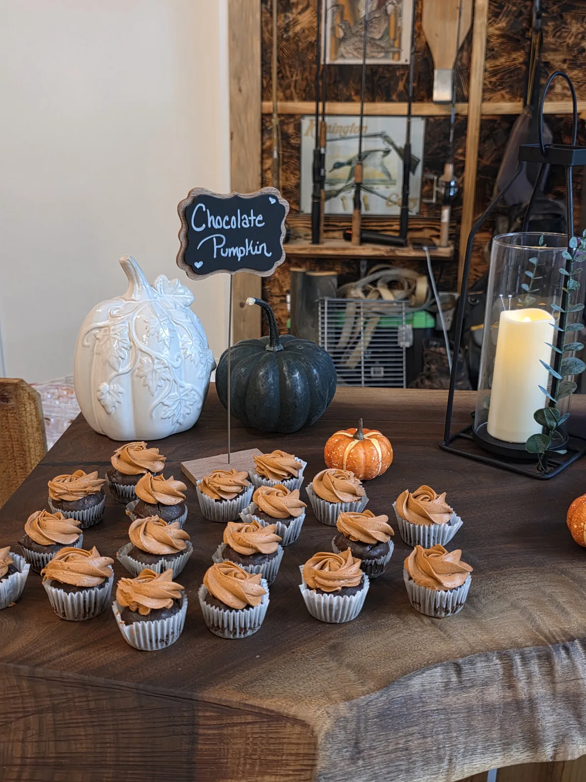 Chocolate pumpkin cupcakes on a rustic wood dessert table with white and green pumpkins and a candle lantern.