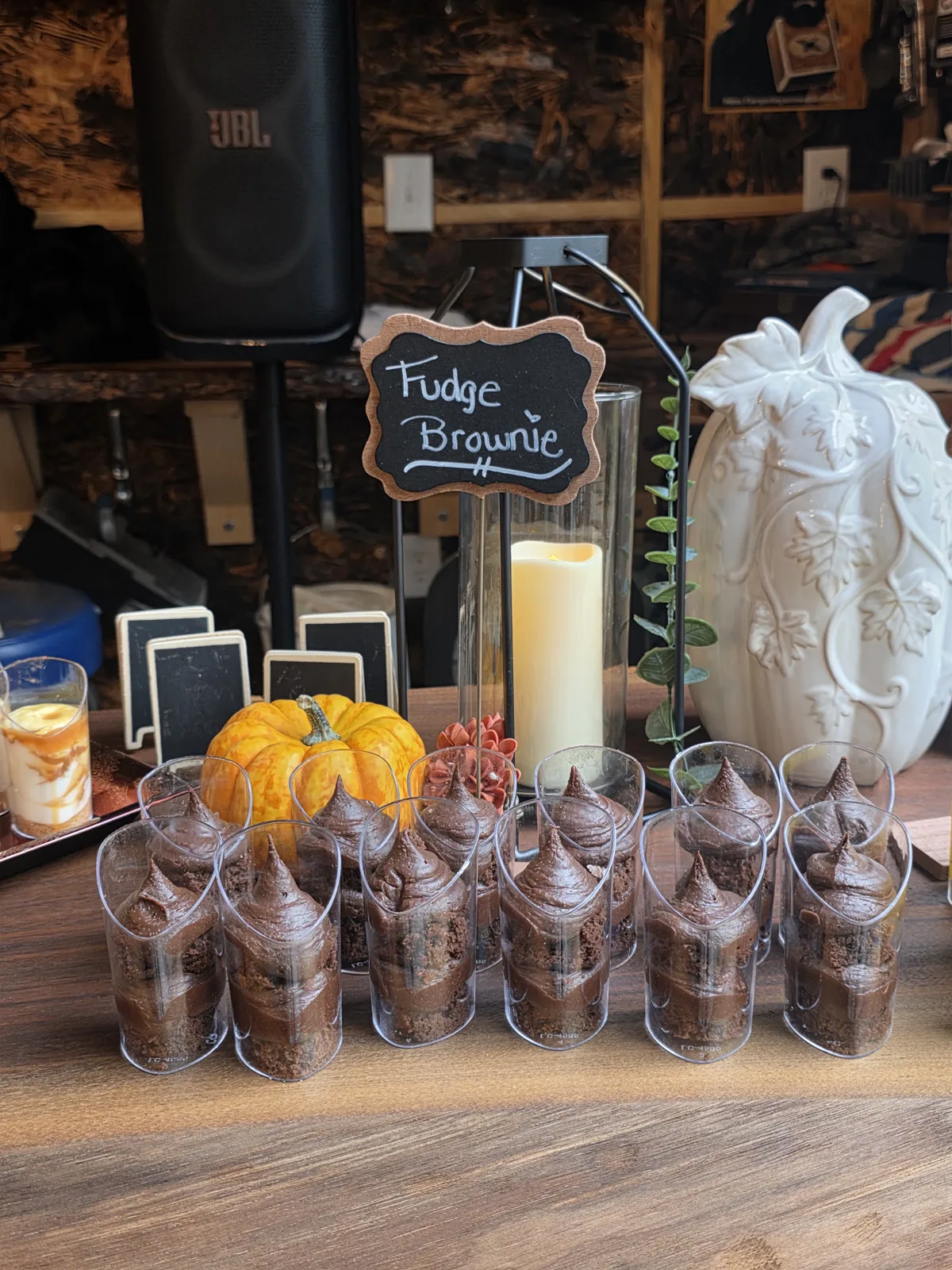 Fudge brownie dessert cups on a wood dessert table with a white pumpkin and a chalkboard sign.