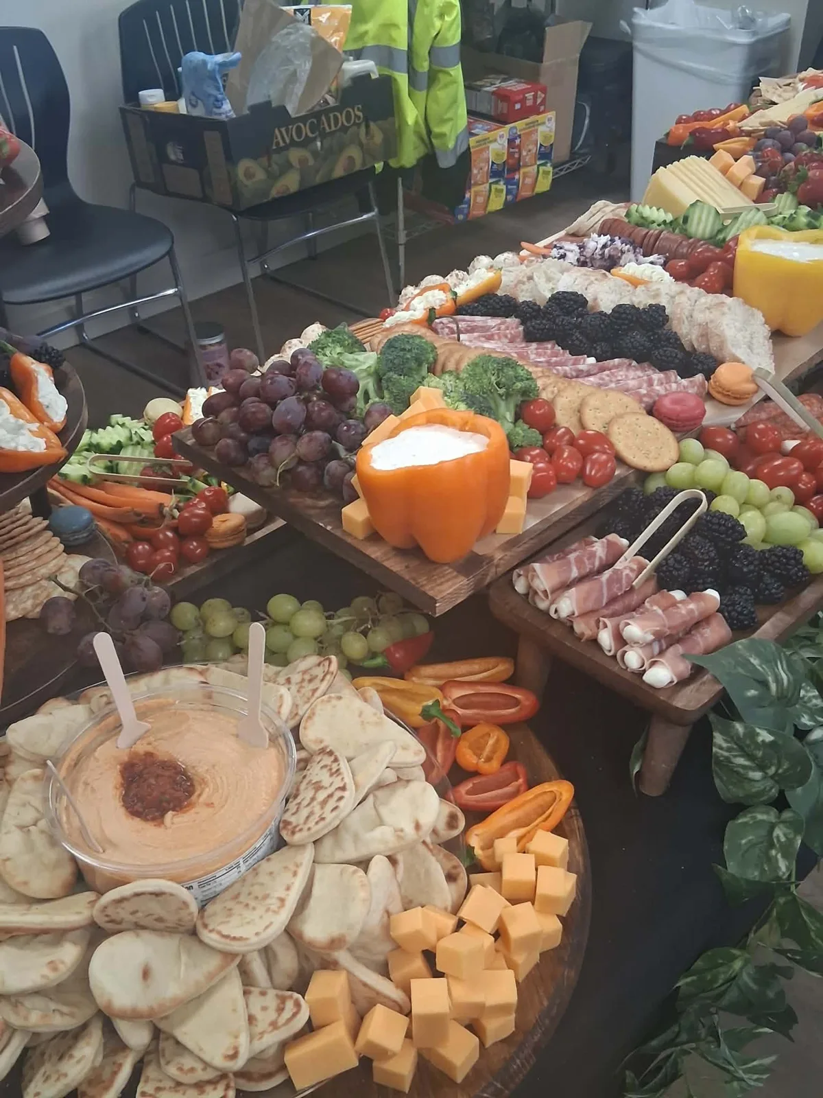 Grazing table with hummus and pita, cheddar cubes, prosciutto wrapped bites, blackberries, grapes, broccoli and a pepper filled with dip.