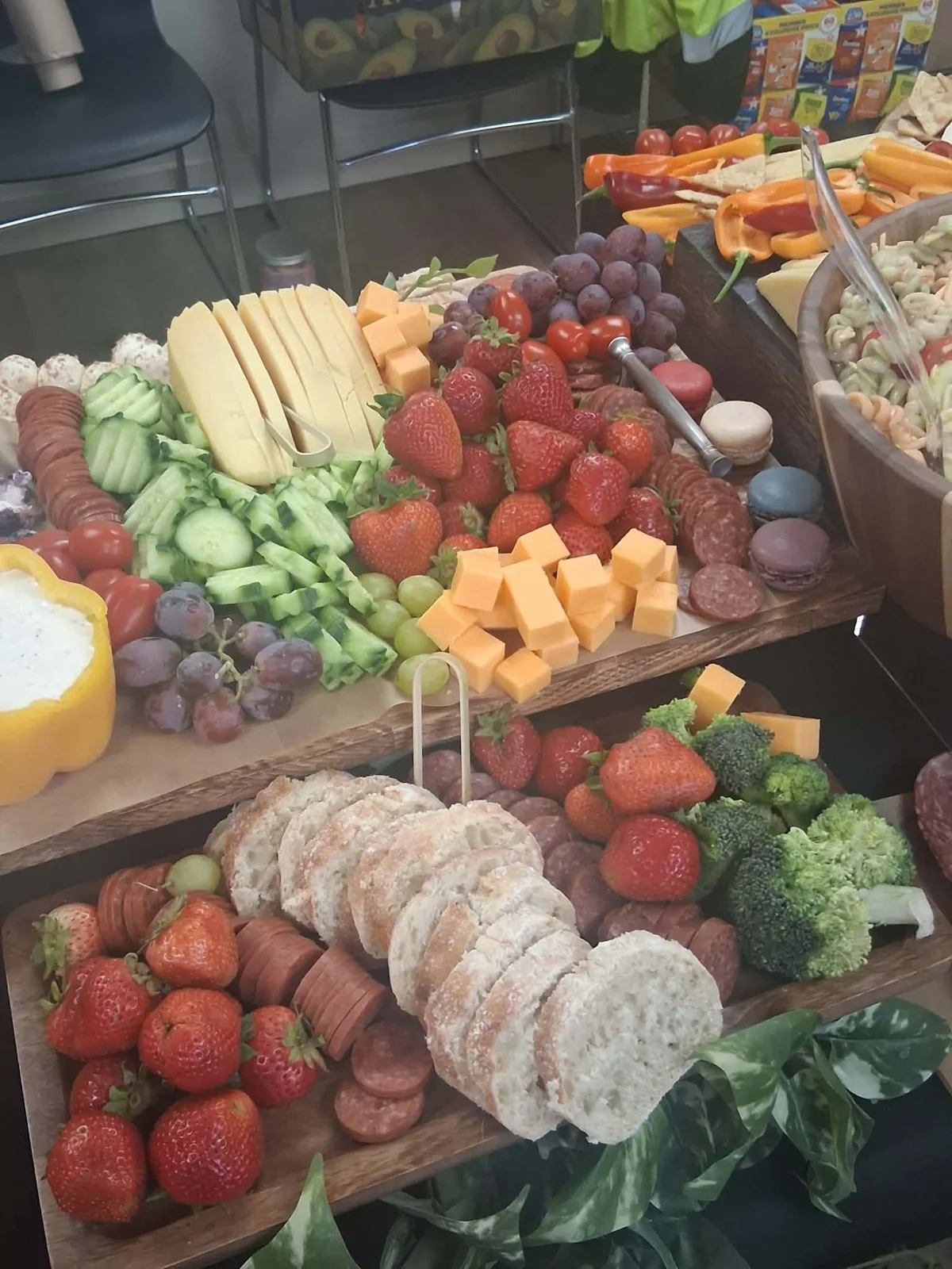 Grazing table boards with strawberries, sliced cheese, cheddar cubes, cucumbers, grapes, summer sausage, macarons and English muffins.