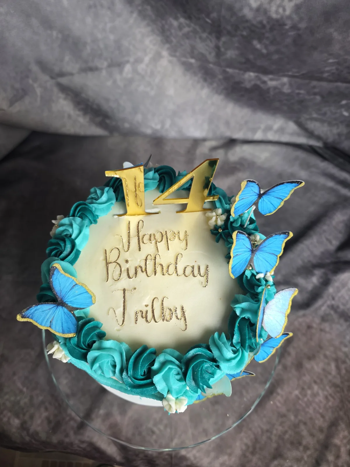 Top view of a teal butterfly birthday cake with a gold 14 topper and Happy Birthday piped in script.