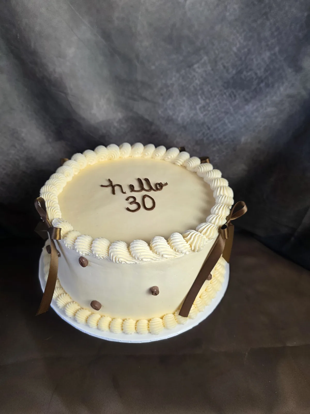 Ivory buttercream 30th birthday cake piped with hello 30, brown ribbon bows and chocolate pearls.