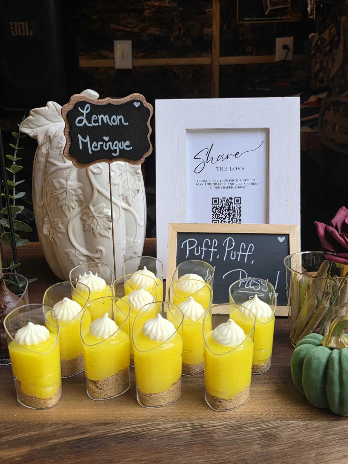 Lemon meringue dessert cups on a dessert table with a chalkboard sign and a white vase.